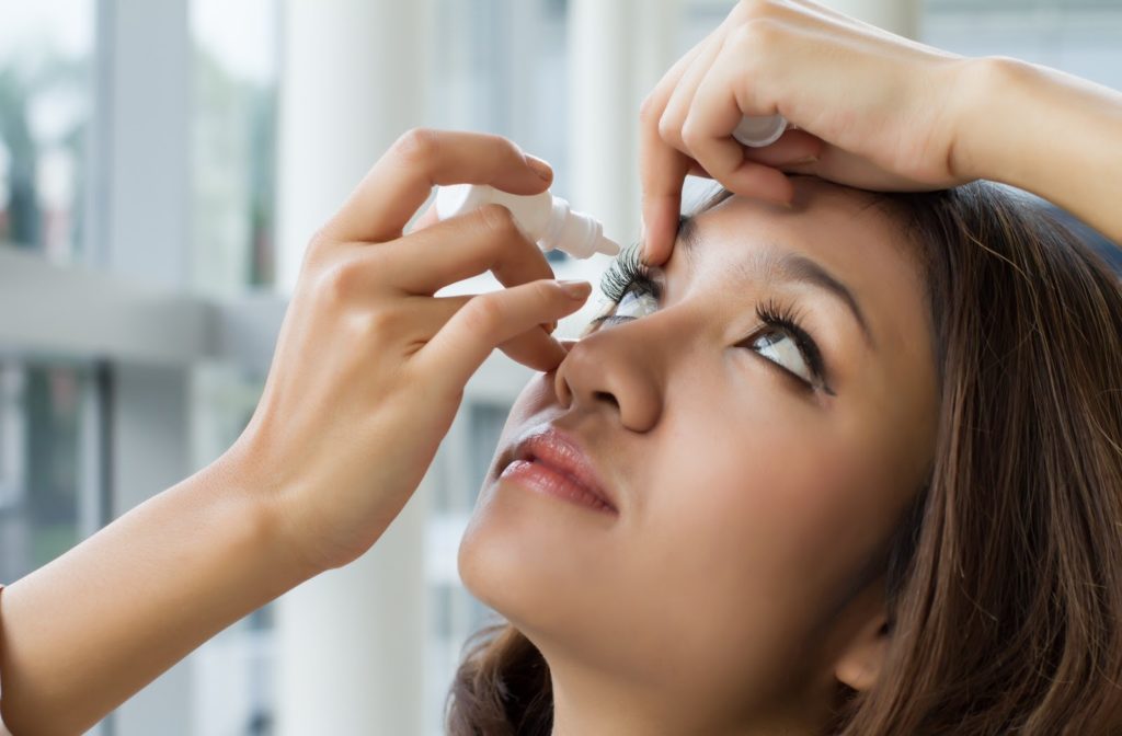 Young woman applying eye drops by opening her eyelid with one hand and using her other hand to squeeze drops into her eye