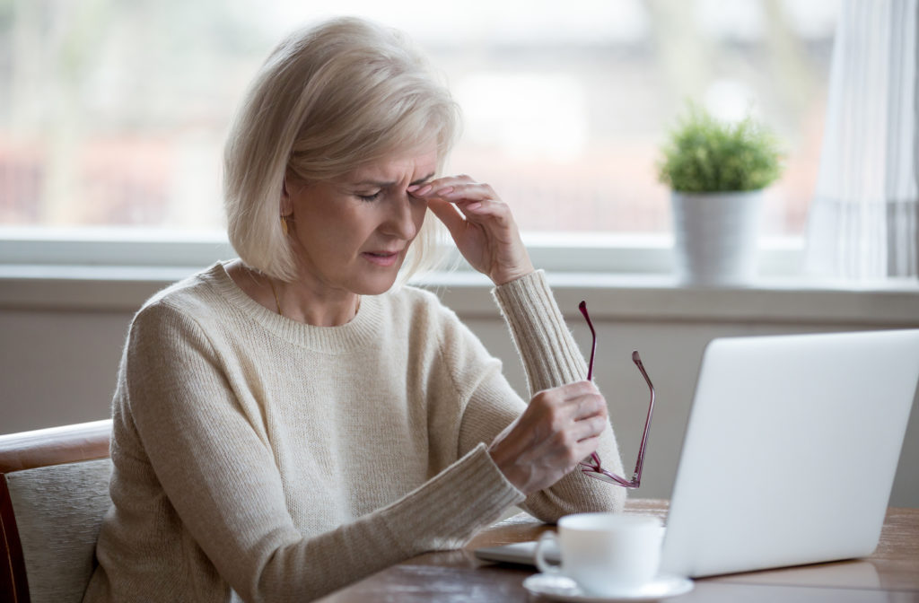 Older women experiencing dry eyes while using her laptop in the morning with cup of tea on table