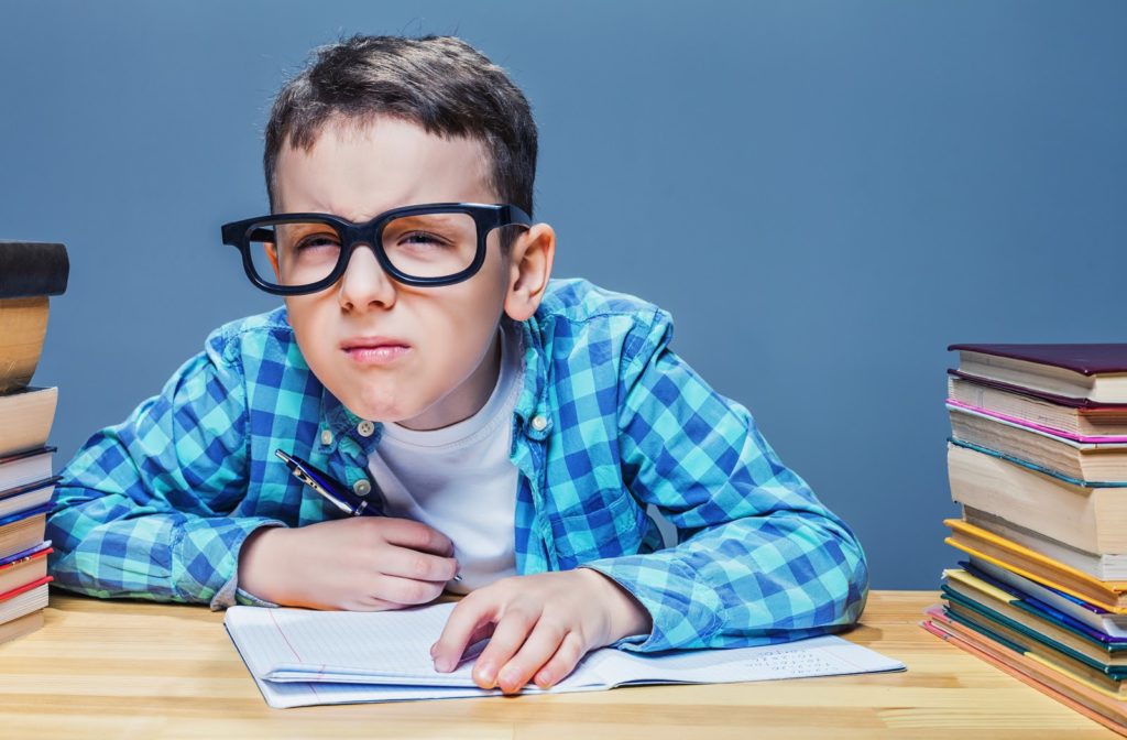 Young boy squinting to see the board at school while taking notes