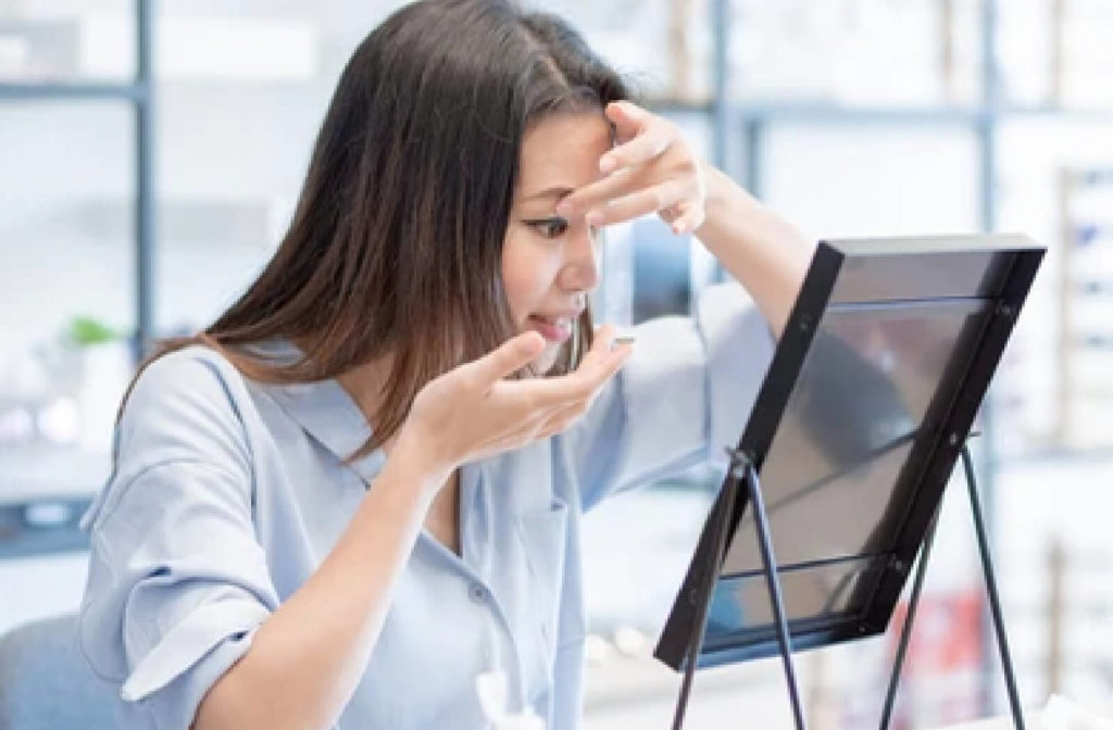 Women at optometrist office opening eye to put in contact lens while looking in mirror