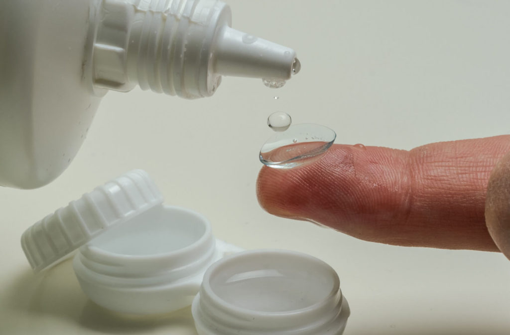 Pour drops of contact lens solution on a contact lens at the tip of a finger.